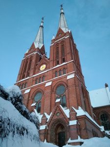 Blick von unten auf das Hauptportal der Kirche mit den beiden Kirchtürmen. Dächer und Umgebung ist schneebedeckt.